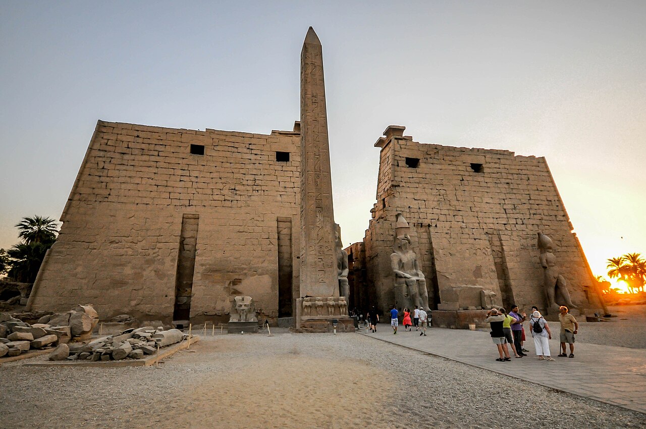https://upload.wikimedia.org/wikipedia/commons/thumb/5/51/The_entrance_pylon_built_by_Ramses_II_with_two_statues_wearing_the_Pshent._Missing_obelisk_in_Paris-_Luxor_Temple_%2814258339141%29.jpg/1280px-The_entrance_pylon_built_by_Ramses_II_with_two_statues_wearing_the_Pshent._Missing_obelisk_in_Paris-_Luxor_Temple_%2814258339141%29.jpg